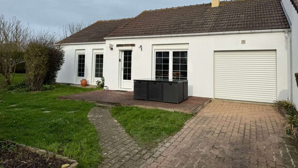 A two-story white house with a tiled roof, a garage door, and a pathway leading to the entrance. - Le Rivage, House with garden near the sea (Saint-Aubin-sur-Mer)