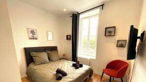A bedroom with a bed, a chair, a window, and a TV. - Apartment "Le Clémenceau", downtown, fully equipped (Saint-Brieuc)