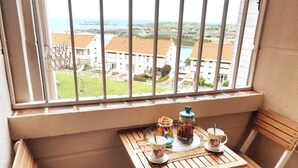 A balcony with a table set for two, overlooking a residential area with houses and a body of water. - Innhome - Jaime del Amo (Suances)