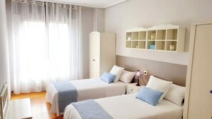 A hotel room with two beds, a wardrobe, a desk, and a window with curtains. - Innhome - Jaime del Amo (Suances)