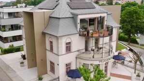 A multi-story building with a rooftop solar panel array, a balcony with outdoor seating, and a sign reading "VILLA VITALIS". - Apartment in villa, sky view, elevator, luxury floor (Bad Hall)