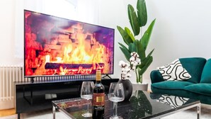 A living room with a TV displaying a fireplace, a bottle of wine, and two glasses on a coffee table.