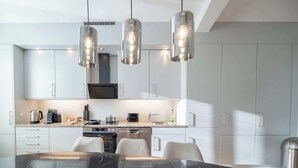 A modern kitchen with white cabinets, a marble countertop, and pendant lighting.