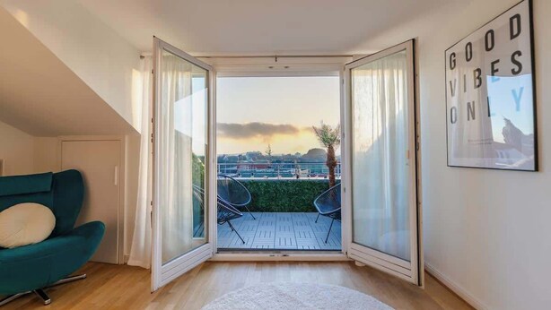 A room with a large sliding glass door leading to an outdoor patio with a view of a cityscape and a sunset.