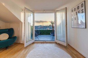 A room with a large sliding glass door leading to an outdoor patio with a view of a cityscape and a sunset.