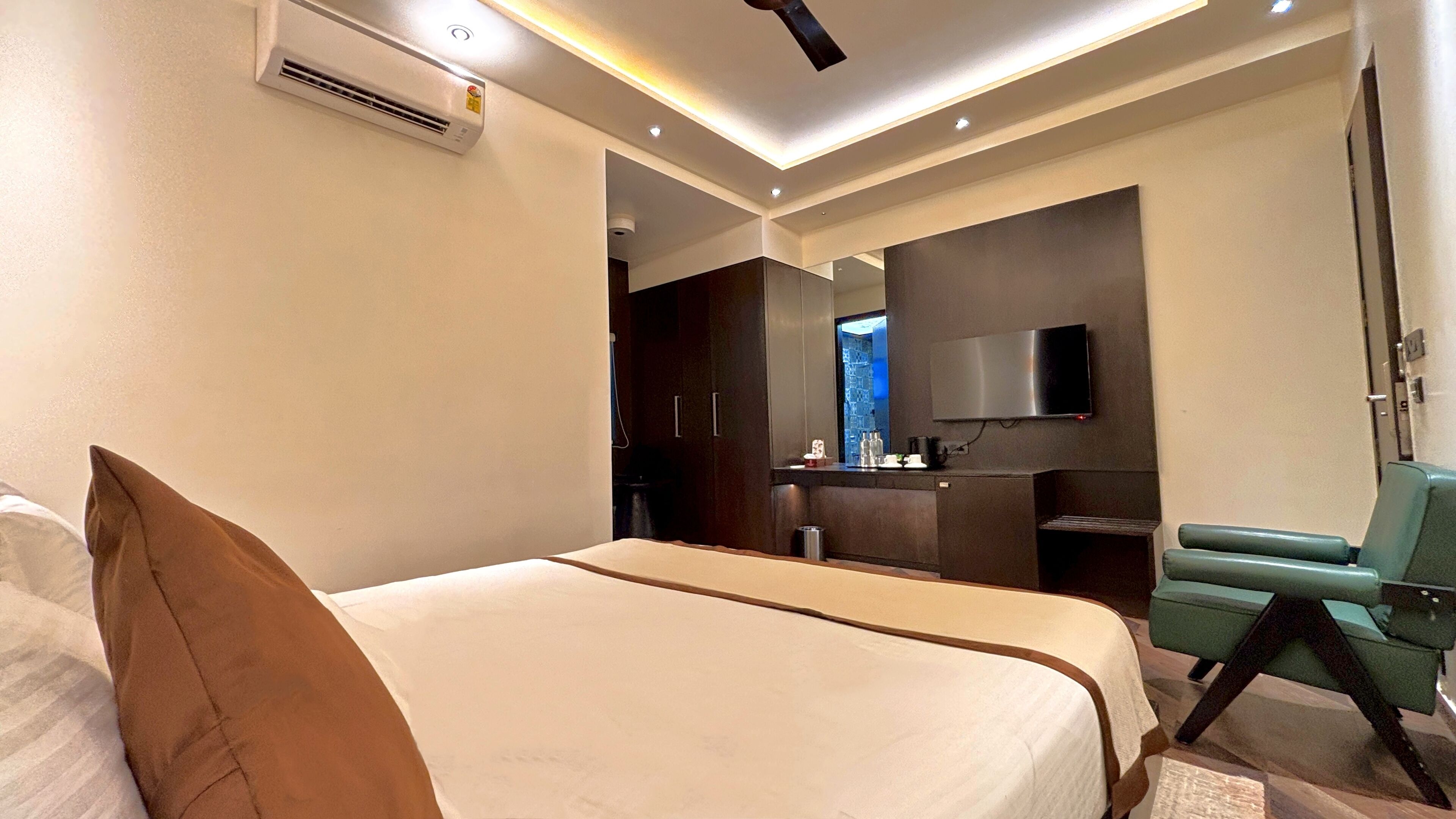A modern hotel room with a large bed, a TV mounted on the wall, a seating area, and a kitchenette.