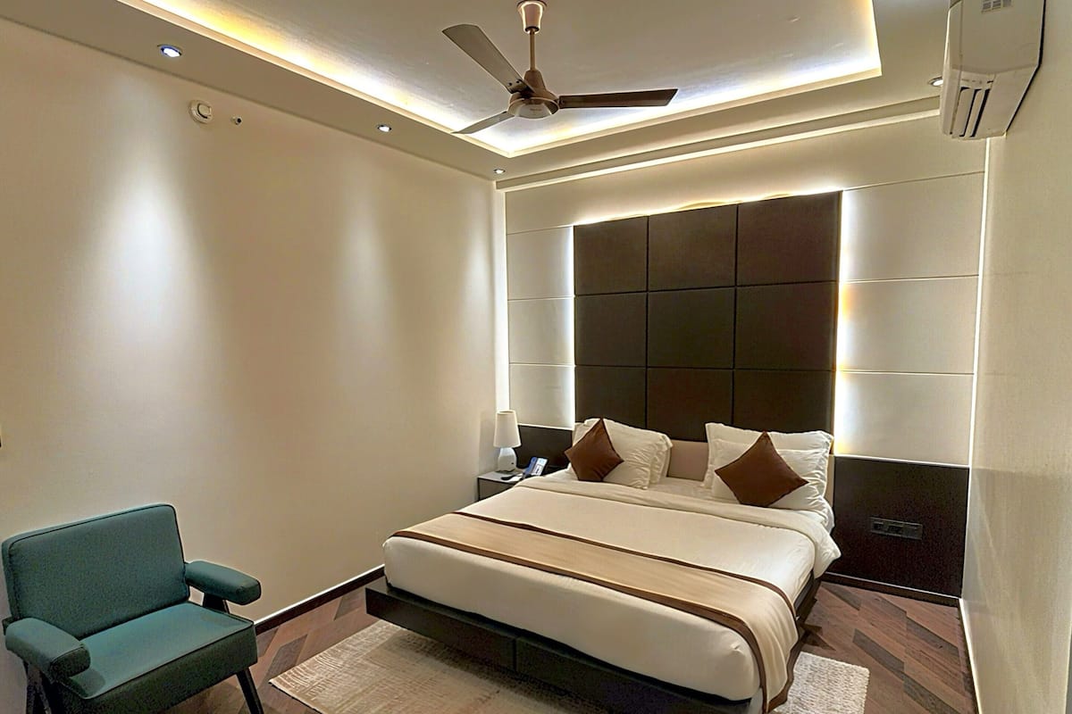 Un dormitorio moderno con una cama grande, ventilador de techo, iluminación empotrada y un sillón verde.