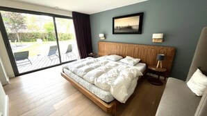 A modern bedroom with a large bed, a wooden headboard, and a view of a patio through a sliding glass door.