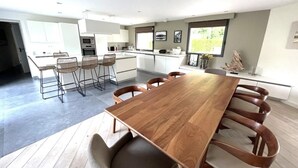 A modern kitchen with white cabinets, a wooden dining table, and bar stools.