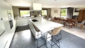 A modern kitchen with a central island, white cabinetry, and a dining area with wooden furniture.