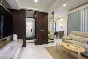 Una sala de estar moderna con un sofá, una mesa de centro y un televisor. Se observa un armario de madera y un espejo.