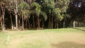 A grassy outdoor area with a wooden bench and a fenced area. - Life Ibiuna space with swimming pool, barbecue and peace (Ibiúna)