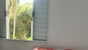 A bedroom with a bed, a window with closed shutters, and a view of trees outside. - Life Ibiuna space with swimming pool, barbecue and peace (Ibiúna)