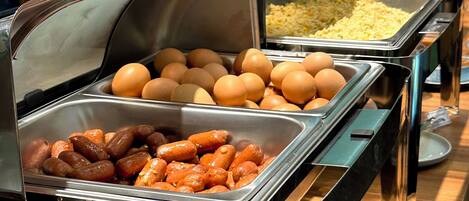 A buffet with various food options including eggs, sausages, and rice dishes.