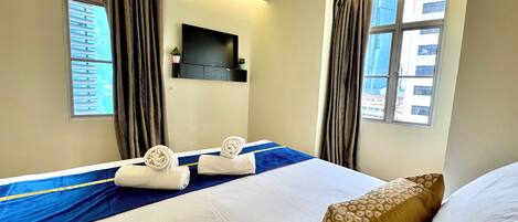 A hotel room with a bed, a flat-screen TV mounted on the wall, and large windows with curtains.