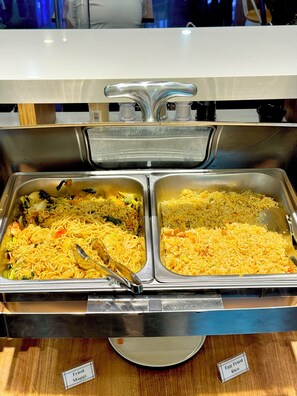 Un bufé con secciones identificadas para maggi frito y arroz con huevo.