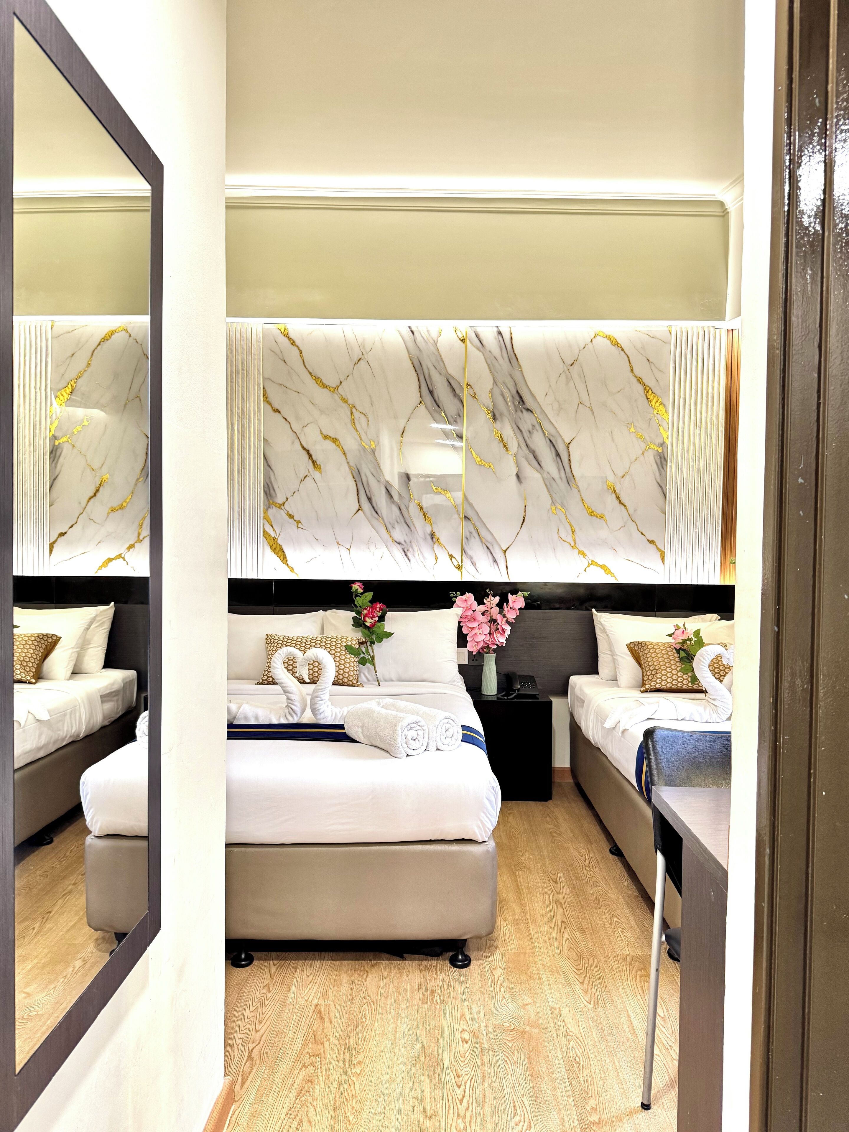 Ein modernes Hotelzimmer mit einem großen Spiegel, einem Kopfschild mit Marmormuster, einem Bett mit weißen Leinen, einem Nachttisch mit Blumen und einem Holzboden.