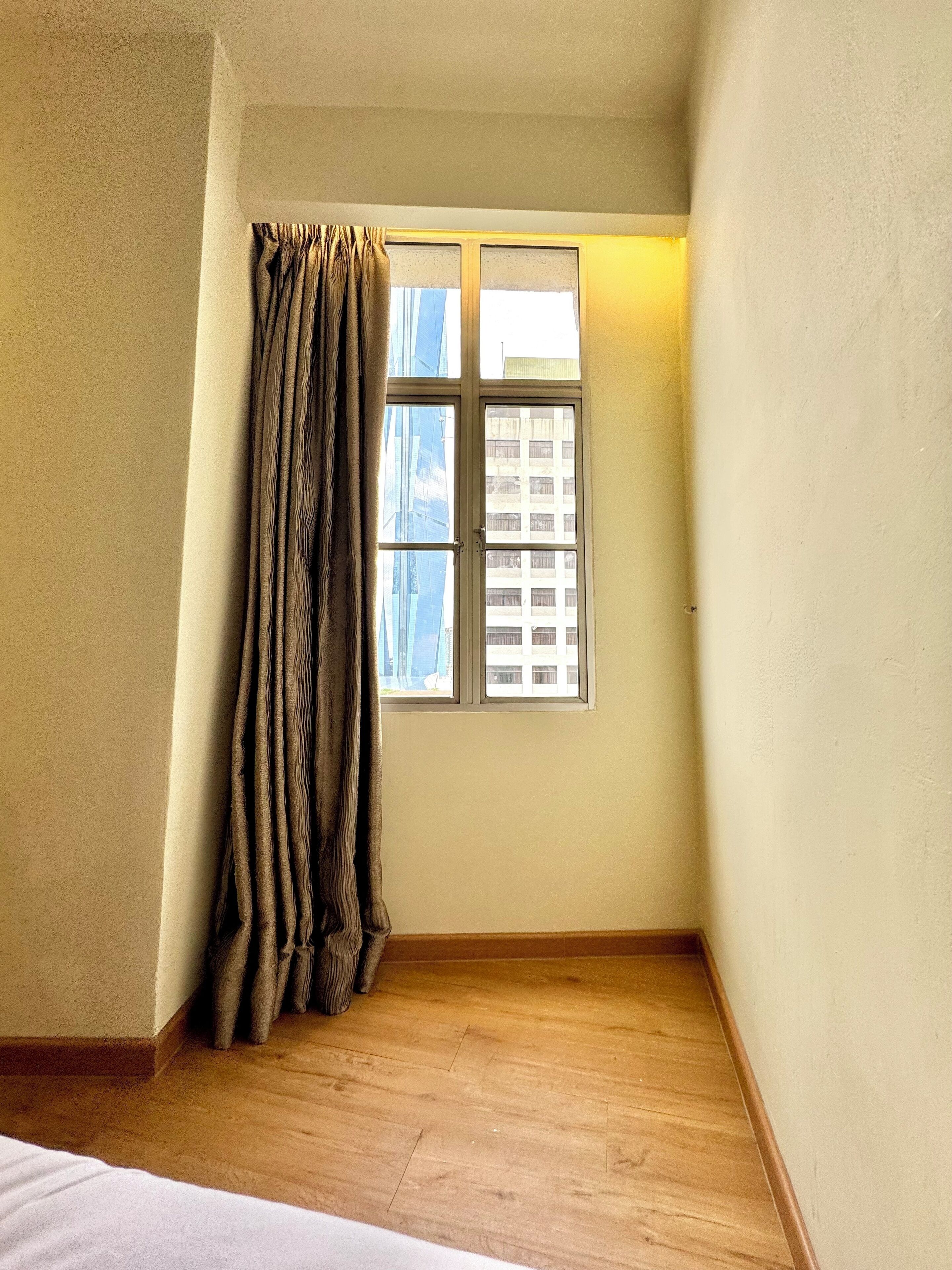 A corner room with a window, wooden floor, and a curtain.