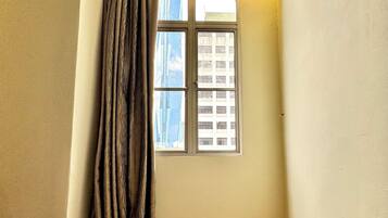 A corner room with a window, wooden floor, and a curtain.