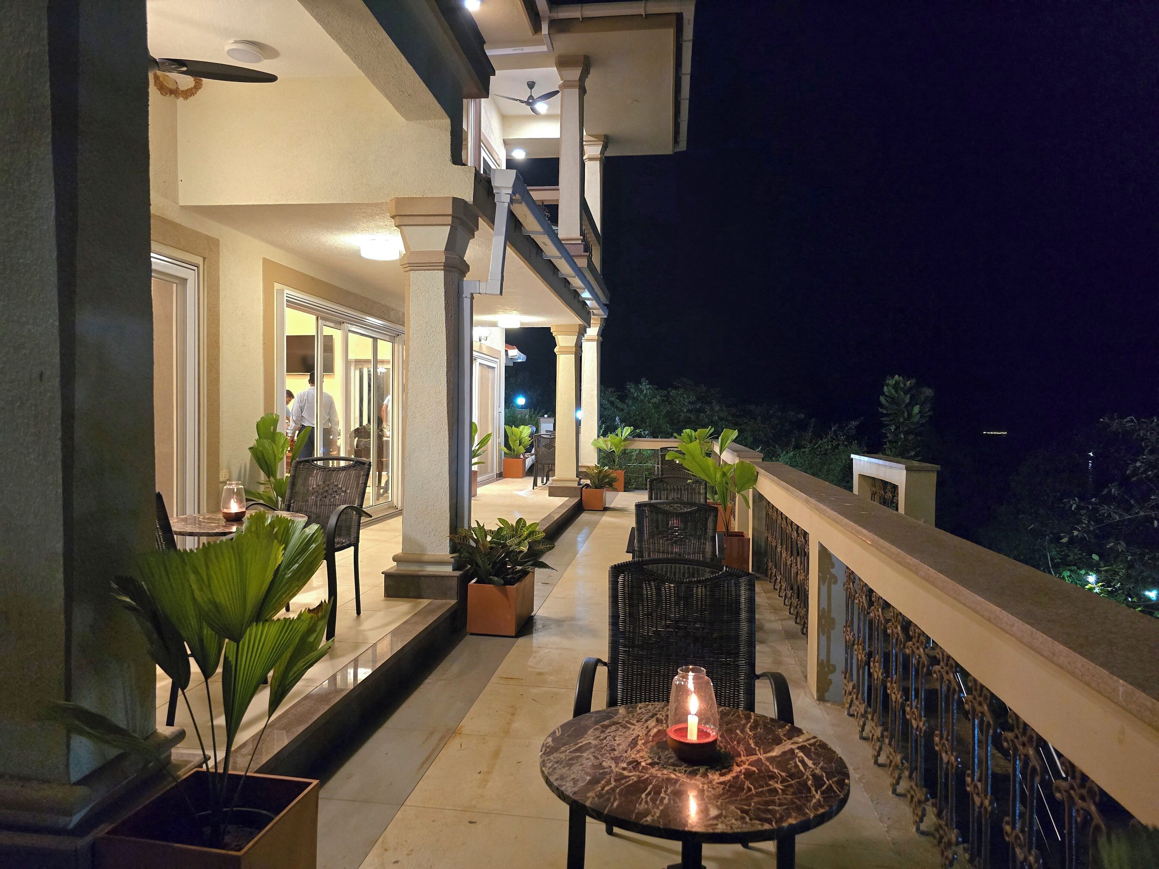 A balcony with a marble table and chairs, potted plants, and a candle.