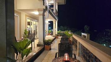A balcony with a marble table and chairs, potted plants, and a candle.