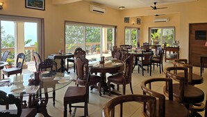 Un comedor amplio con varias mesas y sillas, ventanas grandes que ofrecen vistas a zonas verdes y ventiladores de techo.