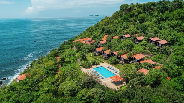 Un complejo turístico costero con varias edificaciones tipo bungalow, piscina y exuberante vegetación.