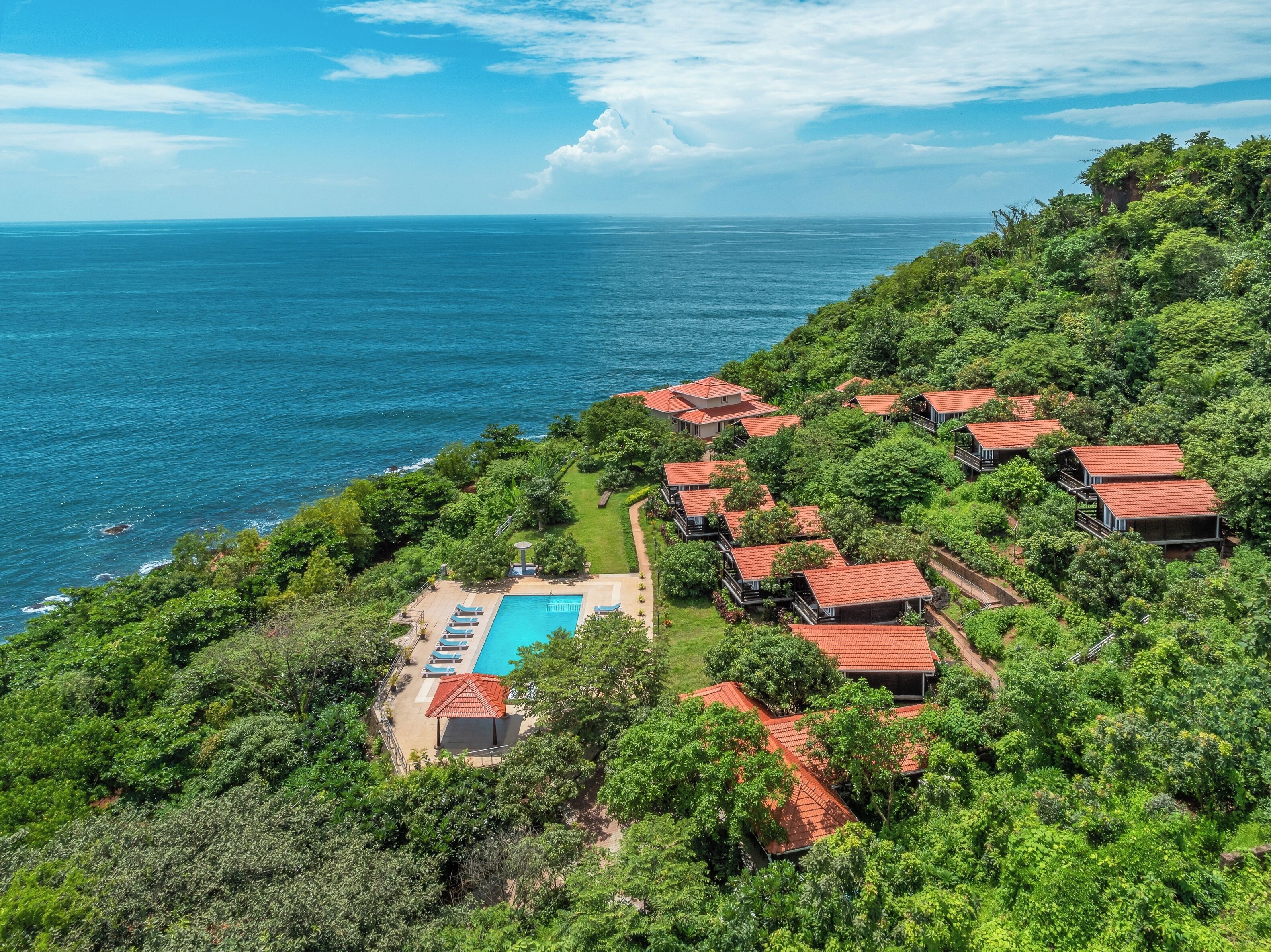 Un complejo turístico frente al mar con varias edificaciones tipo cabaña, una piscina y abundante vegetación.