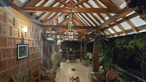 Un interior acogedor y bien iluminado, con vigas de madera, muebles ornamentados y vistas a un follaje exuberante.