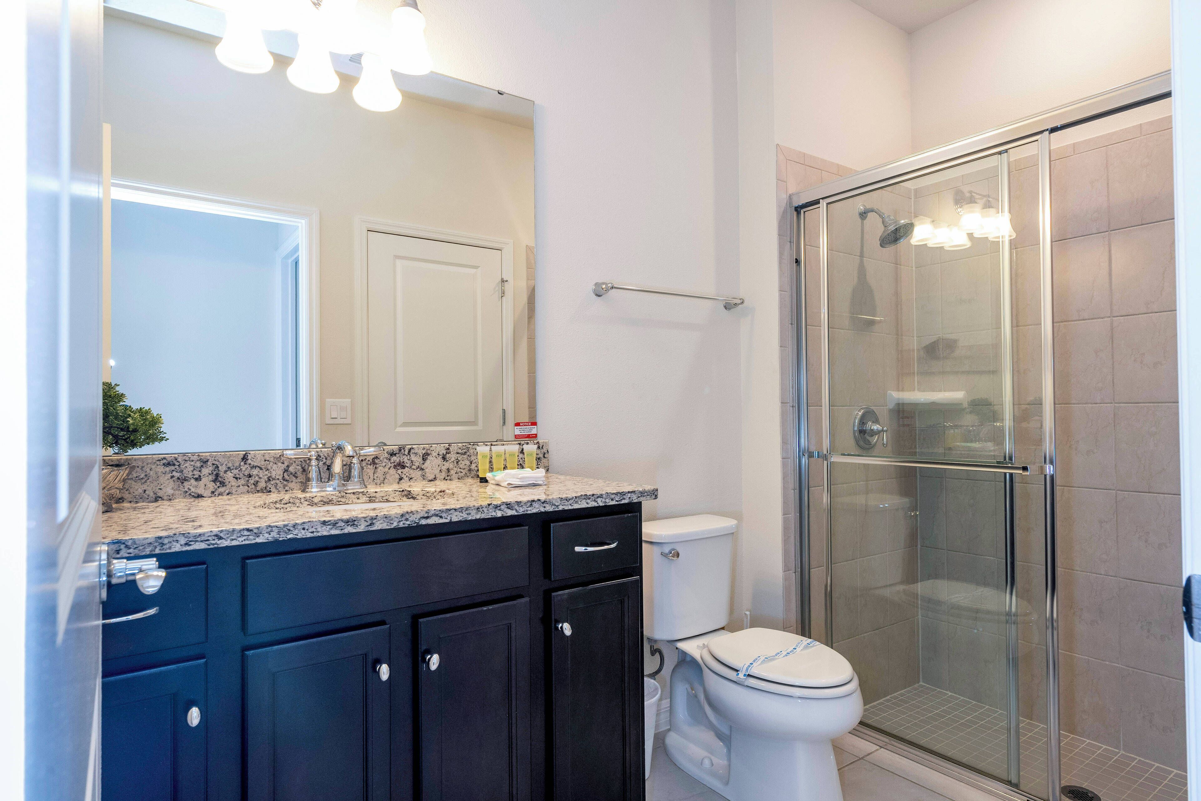 Un baño con ducha envuelta en vidrio, inodoro blanco y muebles oscuros.