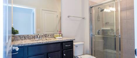 Un baño con ducha envuelta en vidrio, inodoro blanco y muebles oscuros.
