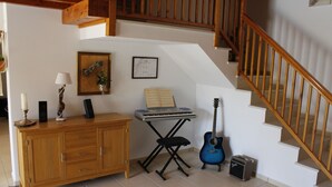 A room with a wooden cabinet, a keyboard, a guitar, and a small amplifier on a tiled floor. - Casa Delbon (Aljezur)