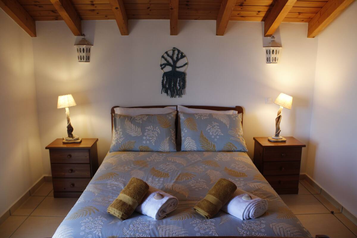 A bedroom with a bed, two nightstands, a wall-mounted tree decoration, and two wall-mounted lamps.