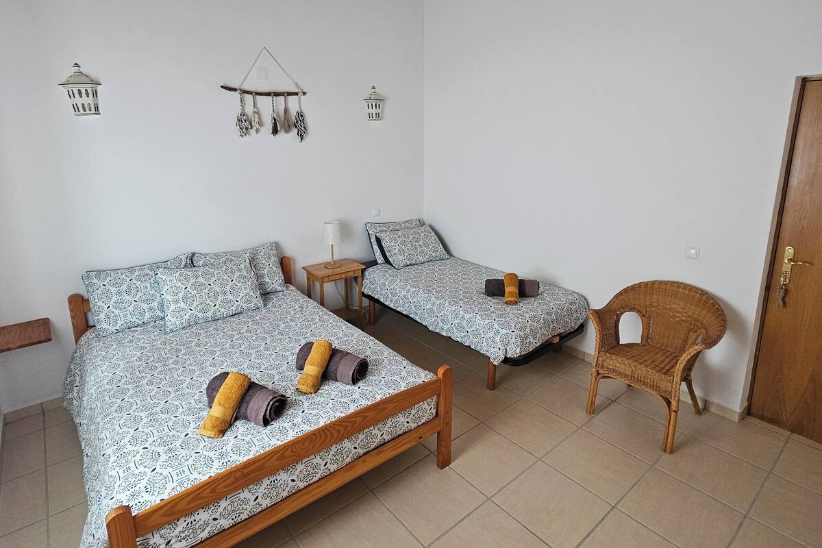 A bedroom with two wooden beds, a small table, and a wicker chair.