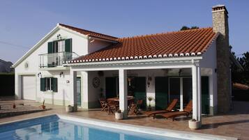 A two-story house with a swimming pool, a balcony, and a patio area with outdoor furniture.