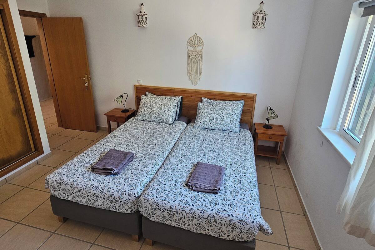 A double bed with patterned bedding, two bedside tables, wall-mounted lamps, and a decorative wall hanging.