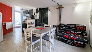 A modern kitchen with a black stove, a dining area with a table and chairs, and a sofa with a black and red patterned cover.