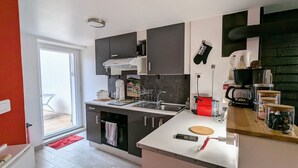 A modern kitchen with a built-in oven, a coffee machine, and a sink. There is a small dining area with a table and chairs visible through the sliding glass door.