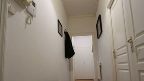 Un couloir étroit aux murs blancs, avec un banc en bois et des portes blanches.