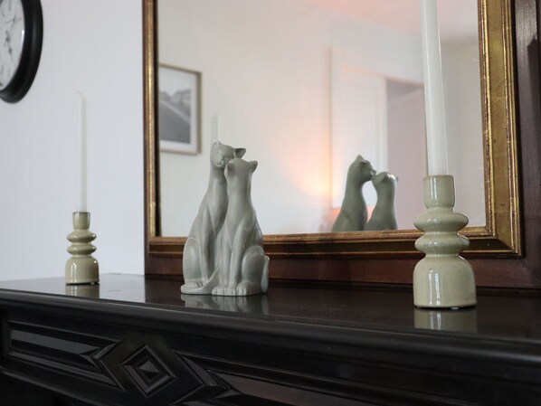 A dresser with a mirror, two candles, and a cat figurine.