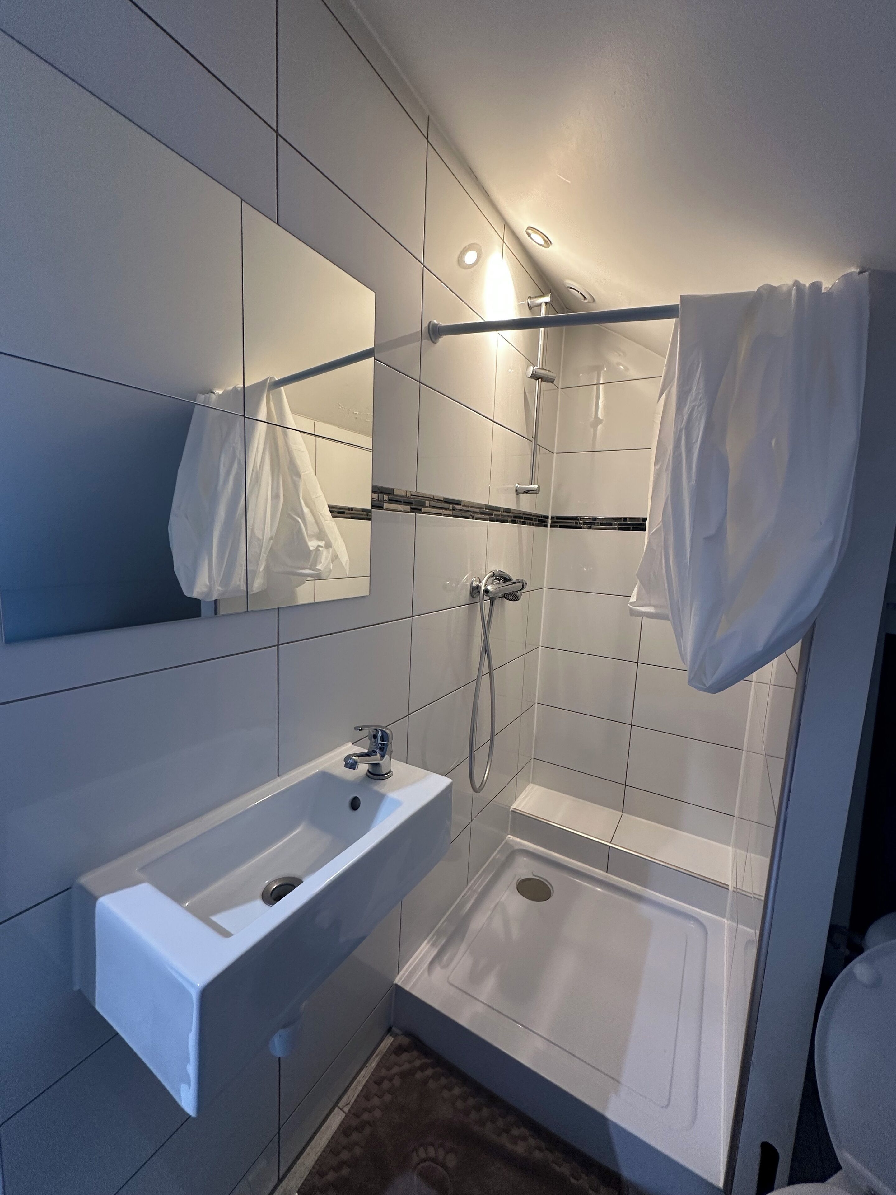 Un baño moderno con un lavamanos blanco, ducha con puerta de vidrio y un espejo grande.
