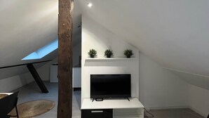 Quarto de sótão moderno com teto inclinado, televisão integrada e estrutura de vigas de madeira.