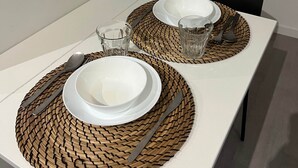Mesa de jantar posta com duas pratos brancos, talheres e copos, com jogos americanos de tecido.