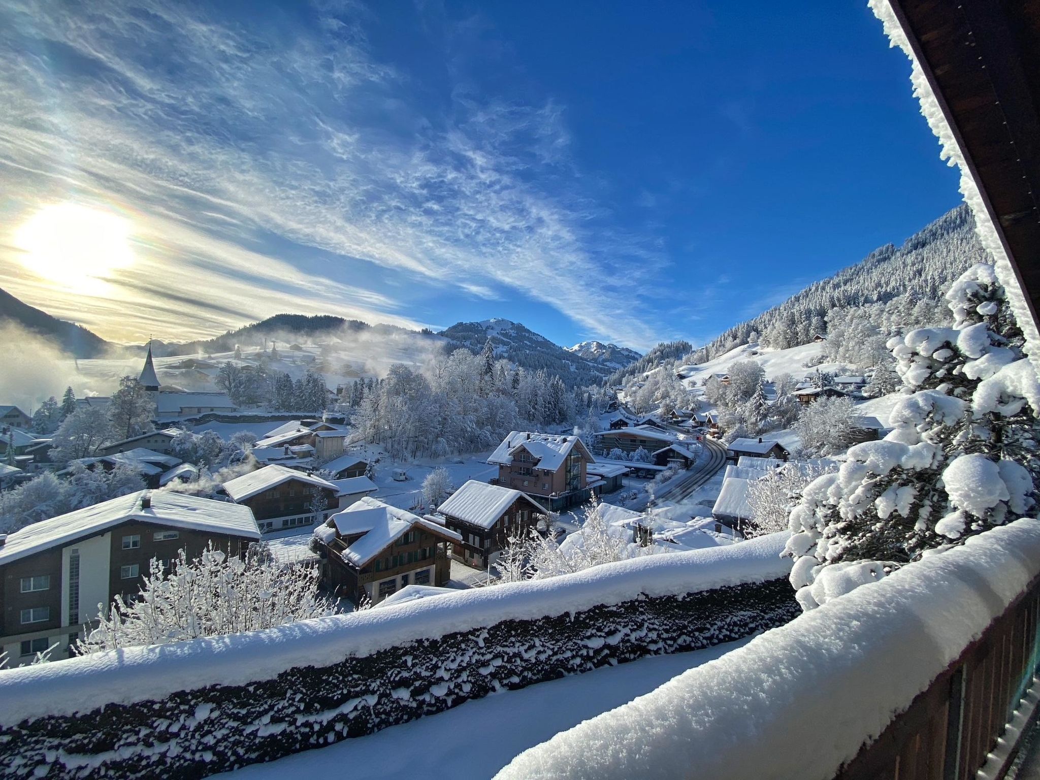 Ein verschneites Dorf mit traditionellen Gebäuden und einer Kirche, umgeben von Bergen.