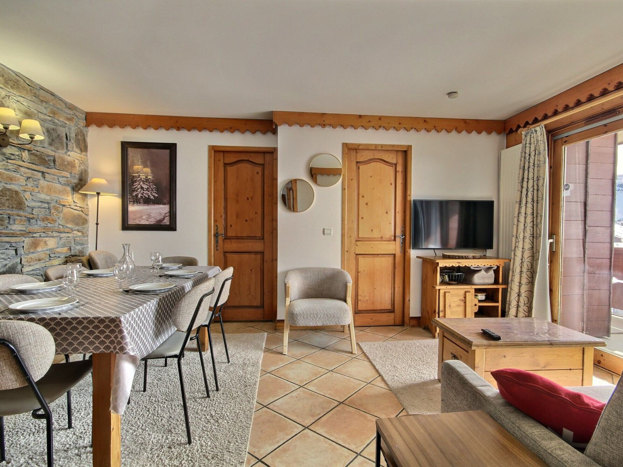 A cozy living room with a dining area, a TV, and a stone wall.