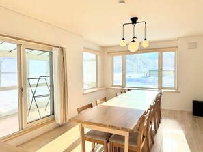 Enjoy meals at the large dining table surrounded by comfortable chairs, with a sliding door leading to an outdoor area.