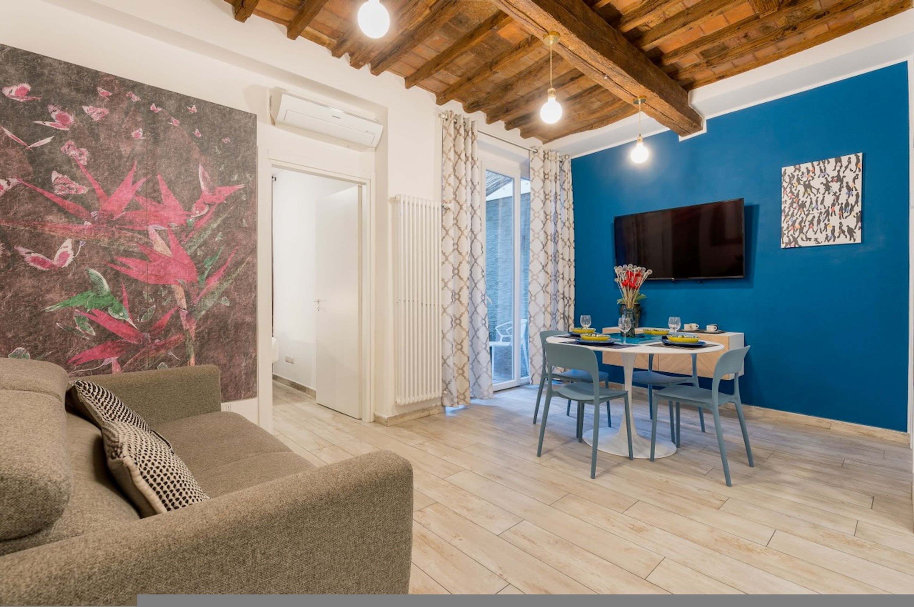 A modern living room with a blue accent wall, a dining area with a table and chairs, and a large painting on the wall.