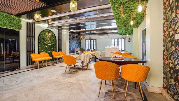 Un comedor moderno con una mesa redonda, sillas naranjas y una pared verde con luces colgantes.