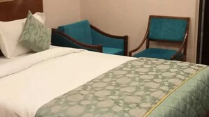 Habitación de hotel con una cama, dos sillas y una lámpara fijada a la pared.