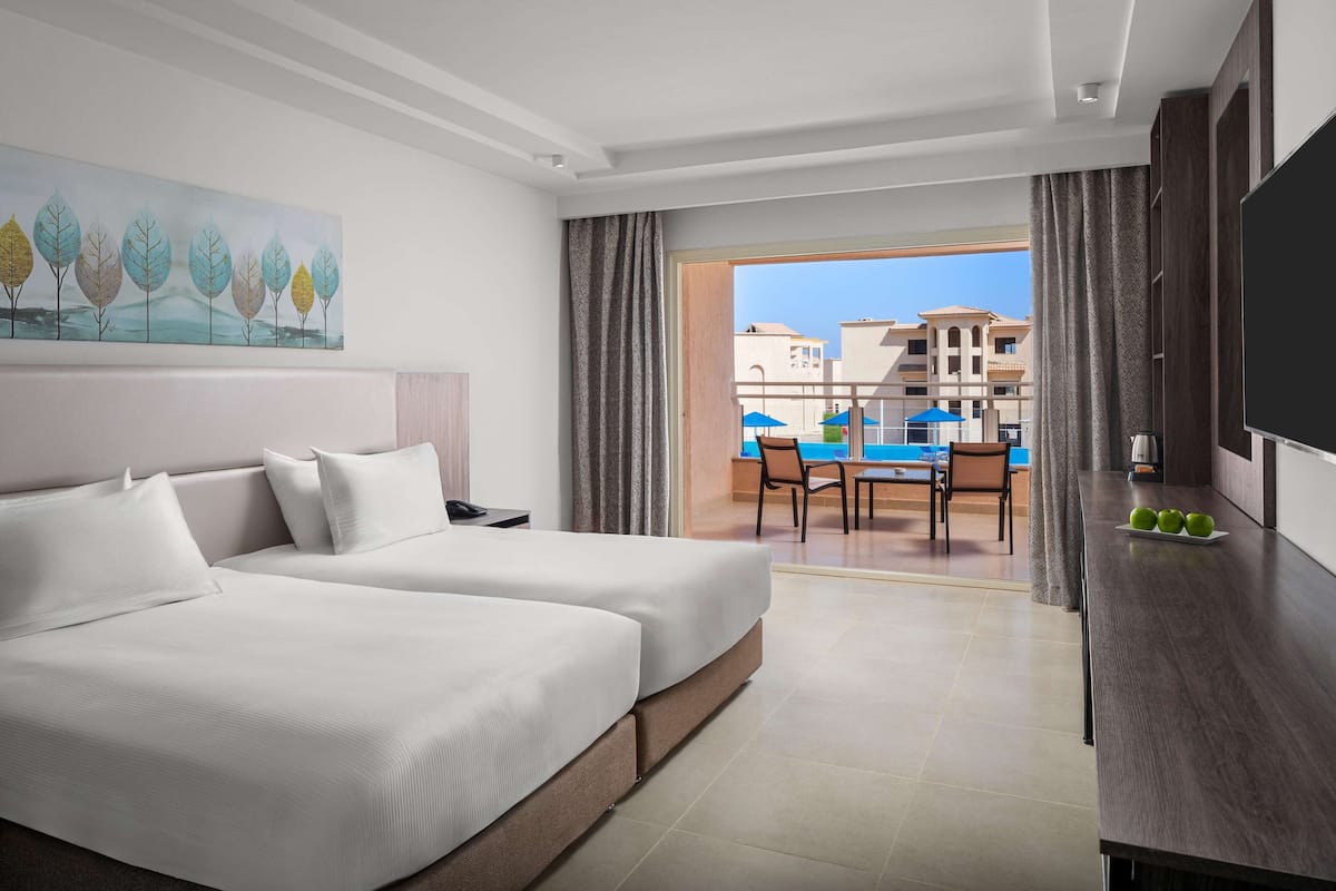 Quarto de hotel com duas camas, televisão e vista para a área da piscina.